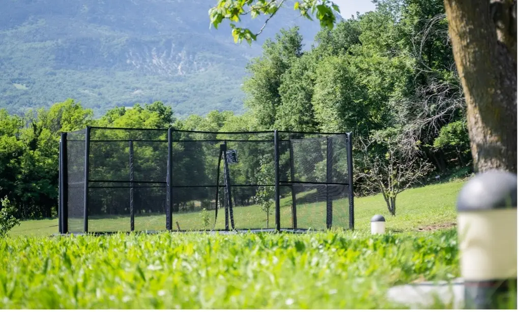 A black metal cage with a central fence stands isolated in a vast green field under a clear blue sky.