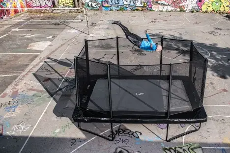 A man leaps into the air on a trampoline in a lively park setting, enjoying a moment of fun and exercise.
